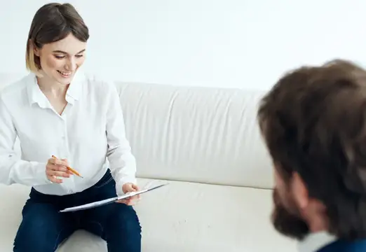 Улыбающаяся женщина с блокнотом беседует с мужчиной на диване