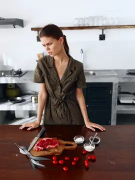 Недовольная женщина смотрит на сырое мясо и ножницы на кухне