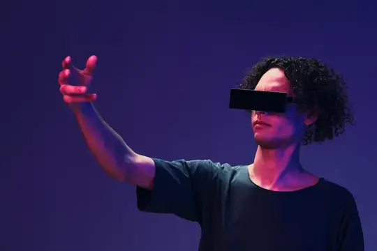 Кудрявый мужчина в VR-очках тянет руку в неоновом свете