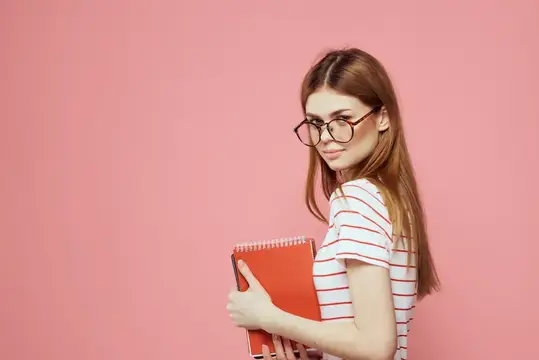 Красивая студентка держит книги, жестикулирует руками на розовом фоне