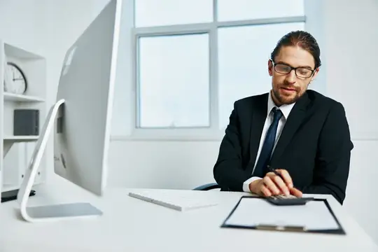 Мужчина в очках и костюме работает за компьютером в офисе