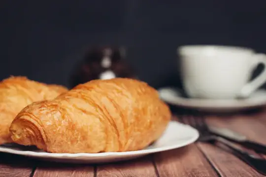 Круассаны на белых тарелках на столе, кухонная утварь, чашка кофе, еда, десерт