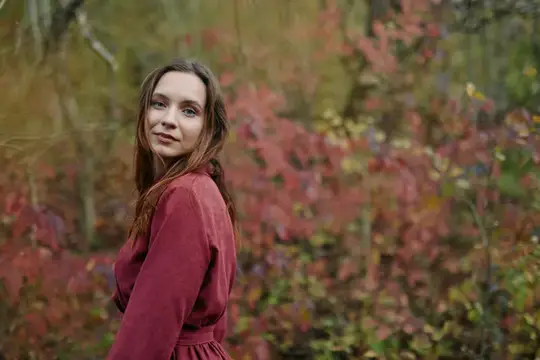 Молодая женщина в бордовом платье на фоне осенних кустов