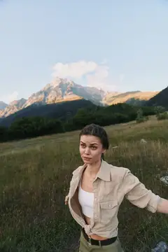 Молодая женщина стоит в горном поле на фоне заката