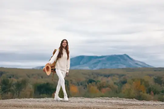 Улыбающаяся девушка с рюкзаком и шляпой на фоне гор