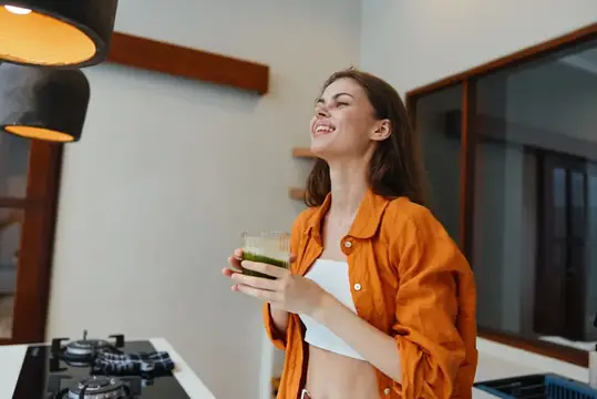 Улыбающаяся девушка с зелёным смузи на светлой кухне