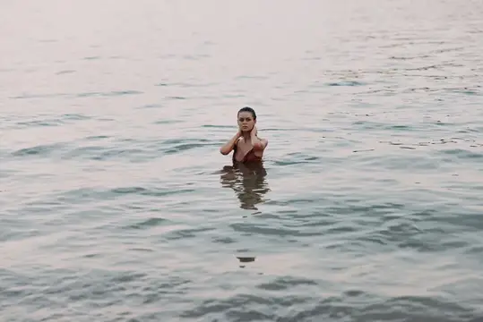 Девушка по грудь в воде спокойно смотрит в камеру