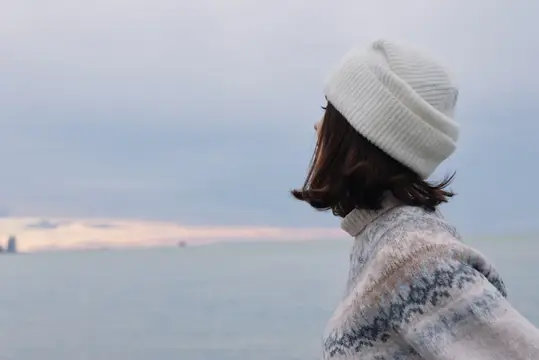 Девушка в белой шапке смотрит на море на закате
