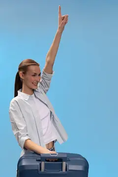 Улыбающаяся девушка с чемоданом поднимает руку вверх на голубом фоне