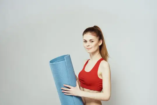 Молодая женщина с синим ковриком для фитнеса на сером фоне