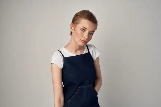 Молодая женщина в тёмном фартуке на сером фоне