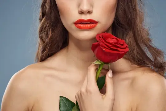 Женщина с красной розой у лица на сером фоне