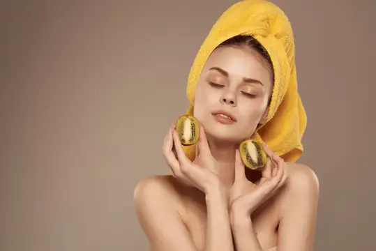 Женщина с полотенцем на голове, ухаживающая за кожей, держит в руке киви, кадр обрезан