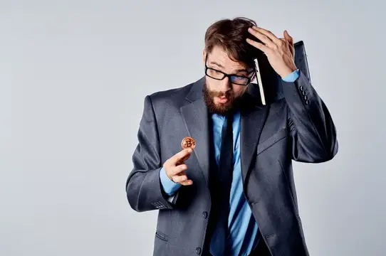 Бородатый мужчина в очках и костюме с удивлением смотрит на монету