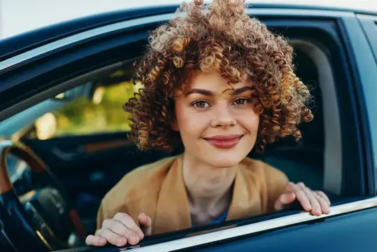 Кудрявая девушка улыбается, выглядывая из окна автомобиля