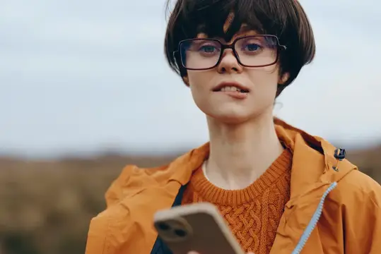 Молодая женщина в очках с телефоном на фоне осеннего поля