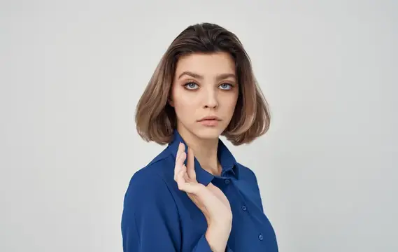Молодая женщина с каре в синей рубашке на сером фоне