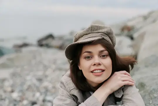 Улыбающаяся девушка в кепке лежит на каменистом берегу