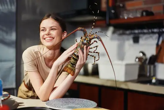 Улыбающаяся девушка держит живого лангуста на кухне