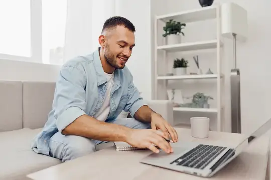 Улыбающийся мужчина работает за ноутбуком на диване