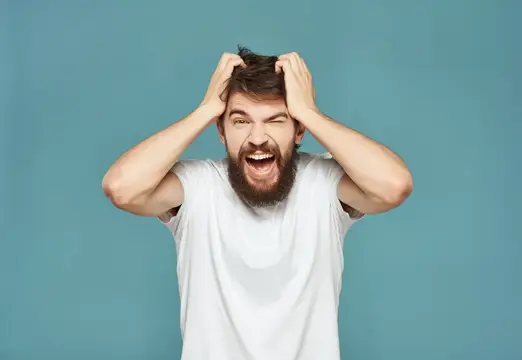 Бородатый мужчина в белой футболке в отчаянии хватается за голову на синем фоне