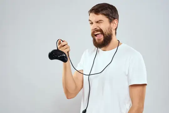 Бородатый мужчина в белой футболке эмоционально играет в видеоигру
