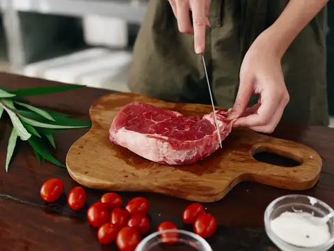 Женщина с ножом в руке нарезает свежий стейк из мяса для запекания на кухне