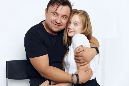Отец обнимает светловолосую дочь на белом фоне