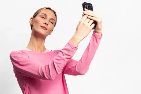 Женщина в розовом топе держит смартфон и делает селфи, изолированная на белом фоне