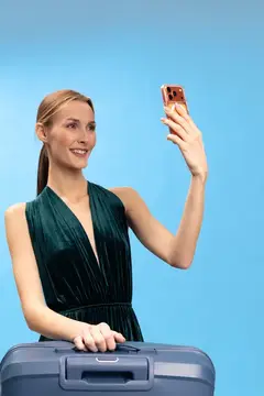 Улыбающаяся женщина с чемоданом делает селфи на голубом фоне