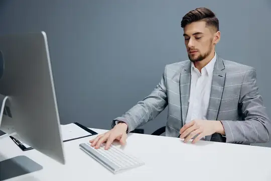 Молодой мужчина в сером пиджаке работает за компьютером в офисе