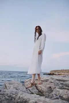 Девушка в белом платье стоит на камнях у моря