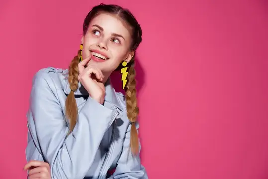 Улыбчивая девушка с косичками и жёлтыми серьгами на розовом фоне