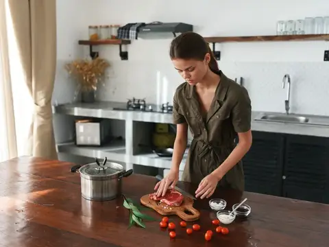 Молодая женщина нарезает мясо на кухне