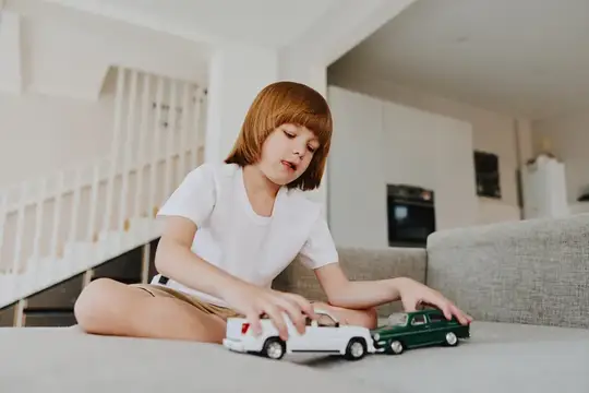 Маленький мальчик играет со своими игрушечными машинками, проявляя воображение и творчество, удобно устроившись на диване