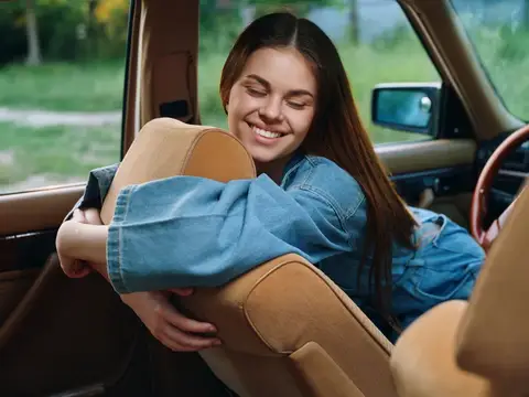 Улыбающаяся темноволосая девушка обнимает сиденье в салоне автомобиля