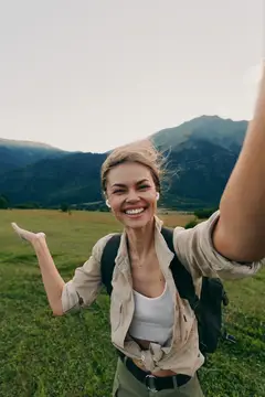 Улыбающаяся девушка с рюкзаком делает селфи на фоне гор