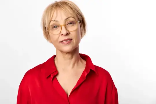 Светловолосая женщина в очках и красной рубашке смотрит в камеру