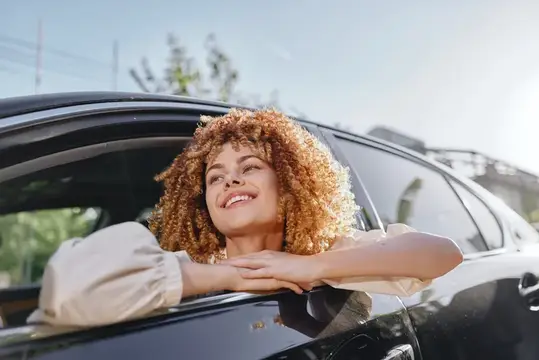 Кудрявая девушка улыбается, высунувшись из окна автомобиля