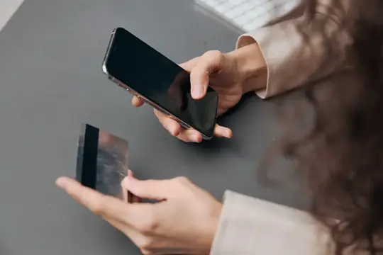 Женщина держит смартфон и банковскую карту над столом