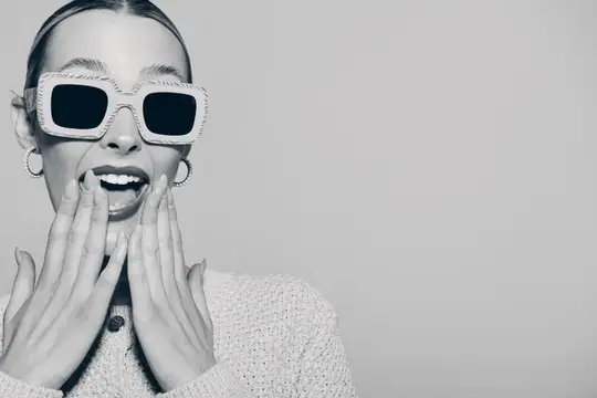 Улыбающаяся девушка в белых солнцезащитных очках закрыла лицо руками