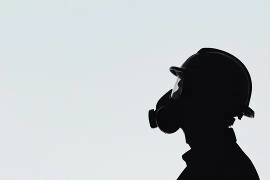 Силуэт мужчины в каске и респираторе на фоне светлого неба