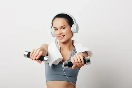 Улыбающаяся девушка в наушниках делает упражнения с гантелями