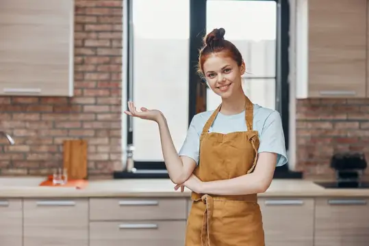 Рыжеволосая девушка в фартуке улыбается на кухне