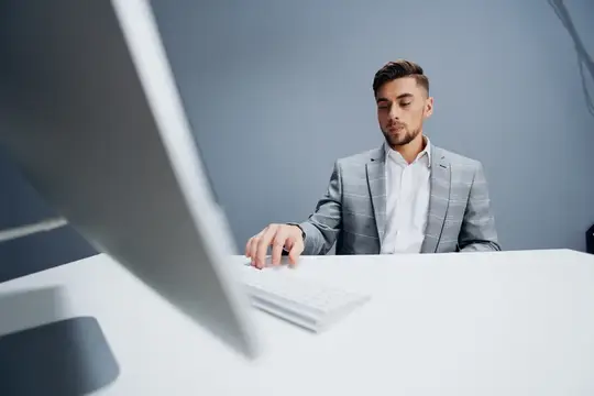 Молодой мужчина в сером пиджаке работает за компьютером в офисе
