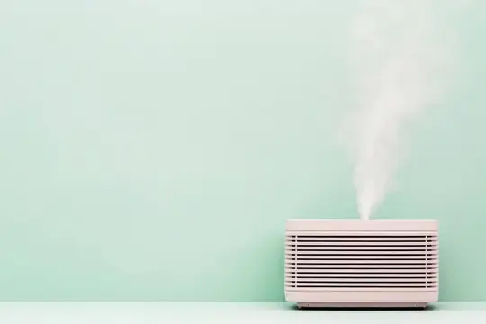 Белый увлажнитель воздуха выпускает пар на фоне мятной стены
