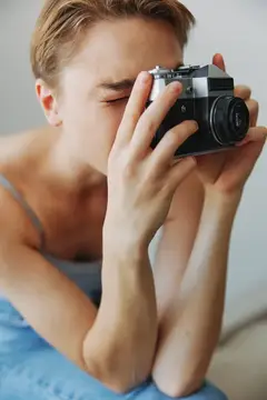 Женщина-фотограф снимает в студии на старую плёночную камеру, сидя дома на диване, портрет на белом фоне, есть свободное место для копирайтинга, внештатный фотограф