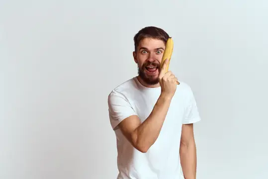 Бородатый мужчина с бананом у уха шутливо удивляется