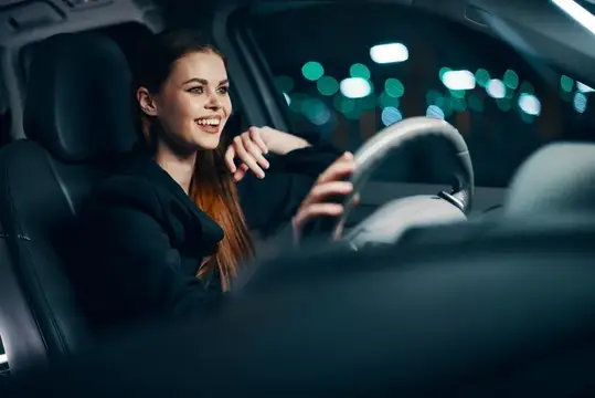 Улыбающаяся девушка за рулём автомобиля ночью