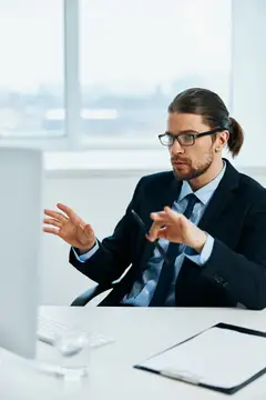 Мужчина с длинными волосами в очках жестикулирует за столом в офисе